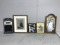 Six assorted wall hangings arranged on floor showing full lot including signs and framed prints and photos.
