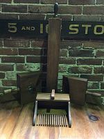 Front view showing all items in the lot. Tall rectangular wooden organ pipe in center with tuning stopper handle. Flanked by two wooden wall pockets with side handles and vertical slats. The cranberry scoop with spaced prongs is centered in front.