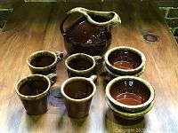 Overview of the full set on wooden surface with pitcher, mugs, and bowls showing brown drip glaze.