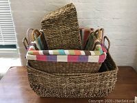 The lot of four woven baskets nested one inside the other shown on a wooden table against a white brick wall. The medium basket has a colorful striped fabric liner.