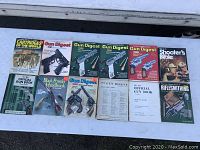Overview of 12 vintage gun and shooting related books laid flat outdoors showing covers worn and several titles visible.