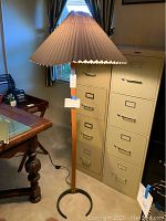 Full view of floor lamp showing wooden base, metal half-moon foot stand and large pleated fabric shade with damage.