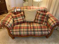 Front view of plaid upholstered Schnadig love seat with three pillows, showing wood base and arm detailing.