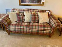 Front view of the couch showing plaid fabric upholstery and decorative pillows in plaid and cream colors.