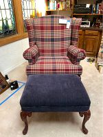 Frontal view of wingback chair and ottoman showing plaid upholstery and wooden queen anne ottoman legs.