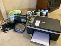 Full view of the printer and accompanying electronics including HP ink cartridges, radios, and Uniden phone