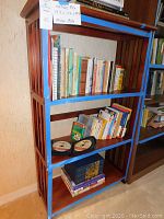 Wooden mission style bookcase filled with various books on three shelves, shown from the front and slightly angled.