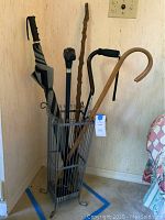 Photo of metal umbrella stand containing walking sticks, canes, and an umbrella.