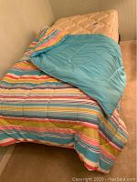 Twin bed with cream Serra mattress and boxspring on metal frame, striped comforter and blue sheets visible.