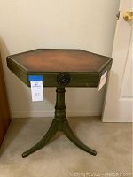 Full view of the six-sided green pedestal table with leather top in corner by wall and door.