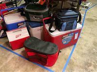 Assortment of coolers including soft and hard plastic coolers stacked on a floor area with blue tape markings