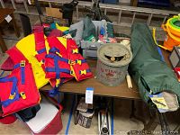 Four life jackets, tackle box, bait bucket, net, and folded recliner chair on table.