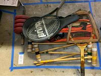 Top view showing two tennis rackets, one vintage wooden and one Prince branded with cover, wooden croquet mallets underneath and a set of red weights