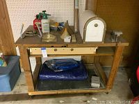 Front view of wooden tool bench with items on top including mailbox, gas can, funnels, vise and small tools. Blue tarp folded underneath.