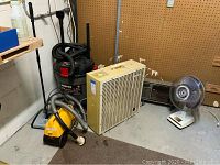 Hoover wet dry vacuum, Eureka Mighty Mite vacuum, box fan, oscillating fan, heater, with pegboard wall and concrete floor