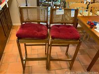 Pair of wooden bar stools with cane backs and red cushions visible.