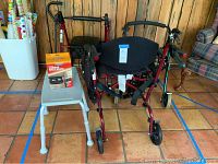 Red seated walker with back support and lumbar back brace box on a white shower chair. Additional seated walkers in background.