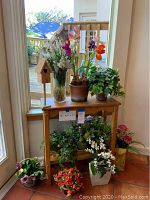 Full view of the wood shelf with assorted artificial plants and flowers placed on and around it, includes birdhouse, glass vase, and multiple flower pots.