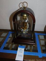 Front view of wooden and glass case showing brass skeleton movement and Roman numeral chapter ring