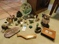 View of assorted small decor items arranged on carpet including ceramic owls, piggy bank, turtles, carved wooden tray, wooden whale, and ceramic dish.