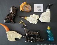 Seven Avon collectible pipes and animal figurines displayed against black background: black dog, cat with fishbowl, budgie, deer with loose antlers, lion, and three pipes shaped like an old man, a horse, and a woman.