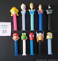 Front view of 10 PEZ dispensers arranged in two rows showing character faces - Princess Peach, Elsa, Cinderella, Superman, Batman, Mario, Yoshi, Spider-Man, Thor, and Minion.