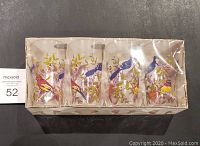 Four glass tumblers in original sealed box with bird and foliage decorations, viewed from front.