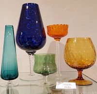 Five Empoli style art glass vases of various colors and styles arranged on a shelf.