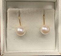 Close-up front view of two round white pearls on 14k gold screw back earrings in a white box.