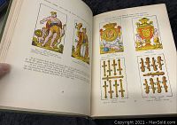 Open book pages showing detailed color illustrations of various playing cards and text explaining their history and symbolism.