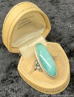 Photo of the sterling silver cocktail ring with a large blue-green stone in a tan jewelry case with 'Rochester' jeweler marking inside the lid.