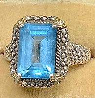 Close-up top view of emerald cut aquamarine set in braided sterling silver bezel with 18K gold prong tips and decorative gold accents