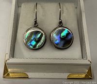 Front view of the pair of round abalone earrings set in sterling silver bezels inside a white jewelry box