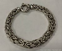 Top-down photo showing full view of the large sterling silver Byzantine style chain bracelet laid flat on a neutral surface with clasp visible.
