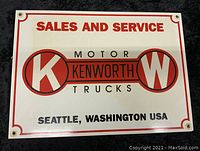 Front view of the enamel Kenworth Trucks sign showing the logo, text, and mounting grommets.