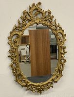 Full front view of the ornate gold oval mirror showing detailed frame and reflective surface.