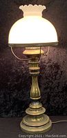 Full view of the vintage brass lamp lit, showing the white glass shade glowing.