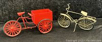 Both tin toy bicycles side by side on a black fabric background, showing size and style comparison.