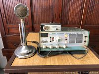 Front view of Robyn T-123B transceiver on wooden table with attached stand microphone.
