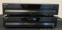 Front view of two stacked black Sony 5 disc CD changer players, showing button controls and digital display panel.