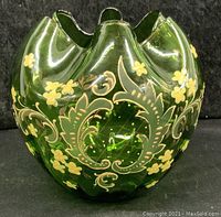 Front view of green blown glass jar showing yellow floral and gold vine hand painted decoration with scalloped top rim.