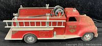 Side view of the vintage red metal firetruck toy showing ladder mounted on side, metal hose reel with rubber hose, and decals 'No. 5'.