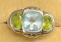 Close-up of the ring's three stones showing aquamarine center and peridot side stones with twisted rope design details on silver band.