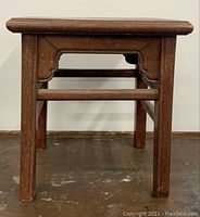 Front view of stool showing rectangular seat, rolled edges, carved apron and cylindrical legs with stretchers