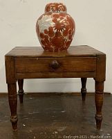 Front view of small wooden table with drawer and round knob, with ginger jar on top