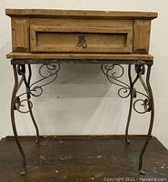 Front view of the wooden end table with metal base and decorative curly metalwork beneath the drawer.