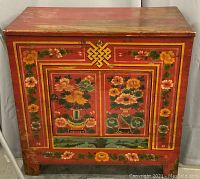Front view of closed cabinet showing painted floral motifs and endless knot