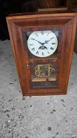 Front view of English mahogany wall clock showing rectangular wooden frame, white Roman numeral clock face, and visible brass gear mechanics behind glass.