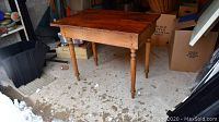 Table showing front and top view, pine wood top with turned legs, situated in garage setting with snow outside.