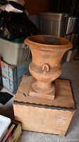 Photo showing full view of large terra cotta urn on wooden box base with flared rim, ring handles, and square pedestal.